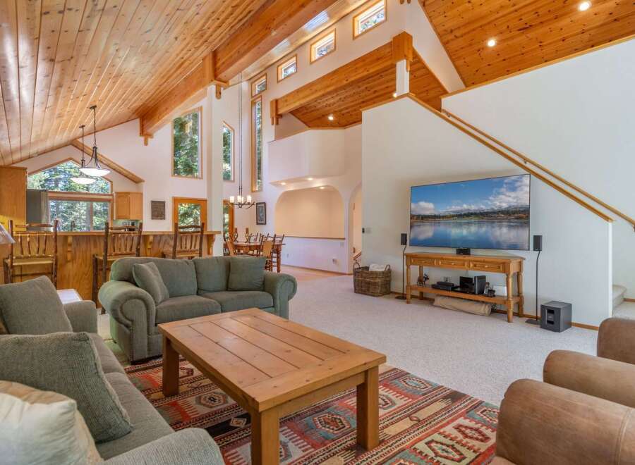 Experience rustic charm in this spacious living area featuring a vaulted wood-paneled ceiling and large windows that flood the space with natural light.