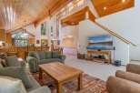 Experience rustic charm in this spacious living area featuring a vaulted wood-paneled ceiling and large windows that flood the space with natural light.