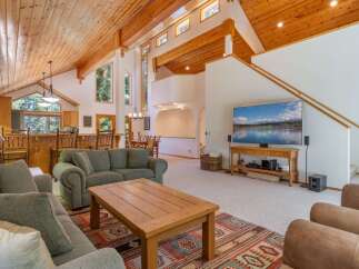 Experience rustic charm in this spacious living area featuring a vaulted wood-paneled ceiling and large windows that flood the space with natural light.