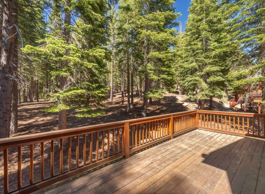 Enjoy the serene mountain lifestyle from this spacious wooden deck, perfect for outdoor entertaining or quiet relaxation amidst a lush pine forest.