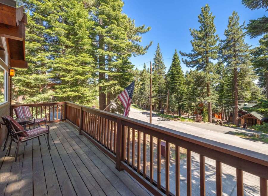 Enjoy the serene mountain setting from this charming cabin's spacious wooden deck, complete with comfortable seating and a picturesque view of tall pine trees.