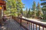 Enjoy the serene mountain setting from this charming cabin's spacious wooden deck, complete with comfortable seating and a picturesque view of tall pine trees.