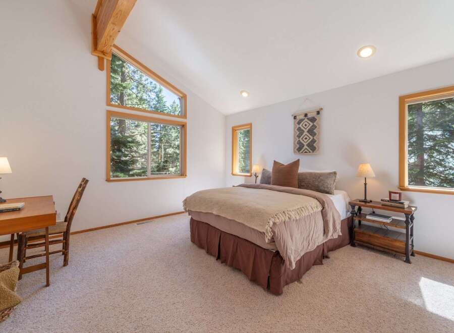 Experience serene living in this charming bedroom, featuring a vaulted ceiling with exposed wooden beams and large windows that offer breathtaking forest views.