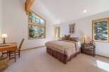 Experience serene living in this charming bedroom, featuring a vaulted ceiling with exposed wooden beams and large windows that offer breathtaking forest views.