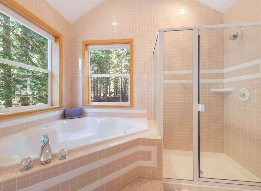 Indulge in relaxation in this luxurious bathroom featuring a spacious corner jacuzzi tub with stunning forest views through two large windows.