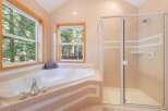 Indulge in relaxation in this luxurious bathroom featuring a spacious corner jacuzzi tub with stunning forest views through two large windows.