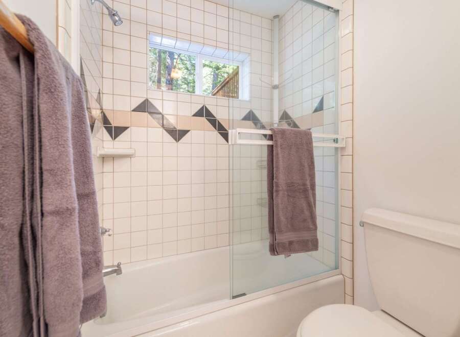 This bathroom features a classic white tiled shower-tub combo with a decorative geometric accent band.