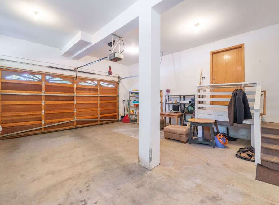 Discover ample storage and functionality in this spacious garage, featuring a large wooden garage door and convenient shelving units.
