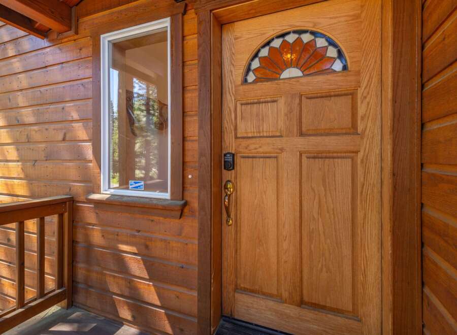 Step into this charming cabin-style home, featuring a beautiful wooden door with a stained-glass transom window that adds a touch of elegance.