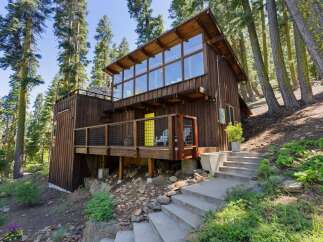 Nestled amidst tall trees, this charming wooden cabin offers a unique architectural design with a striking wall of windows on the upper level, flooding the interior with natural light.