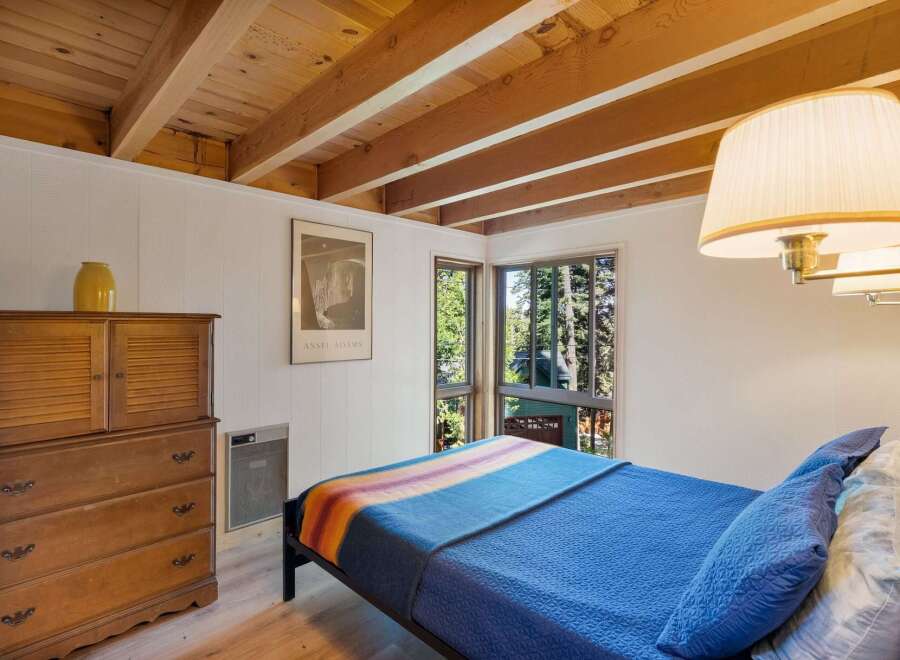 This cozy bedroom features a rustic wooden dresser and a comfortable bed adorned with a colorful striped blanket.