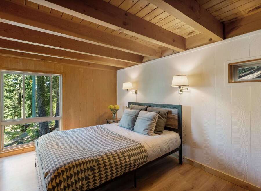 Experience serene living in this charming bedroom, featuring a cozy bed adorned with a geometric-patterned blanket and plush pillows.