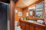 This charming bathroom features a rustic wooden vanity with a built-in sink, complemented by warm wood paneling and a sloped ceiling.