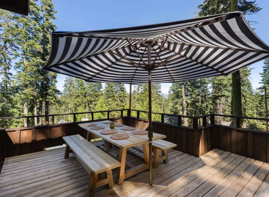 Enjoy al fresco dining on this spacious wooden deck, complete with a picnic table, benches, and a stylish striped umbrella for shade.