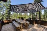 Enjoy al fresco dining on this spacious wooden deck, complete with a picnic table, benches, and a stylish striped umbrella for shade.