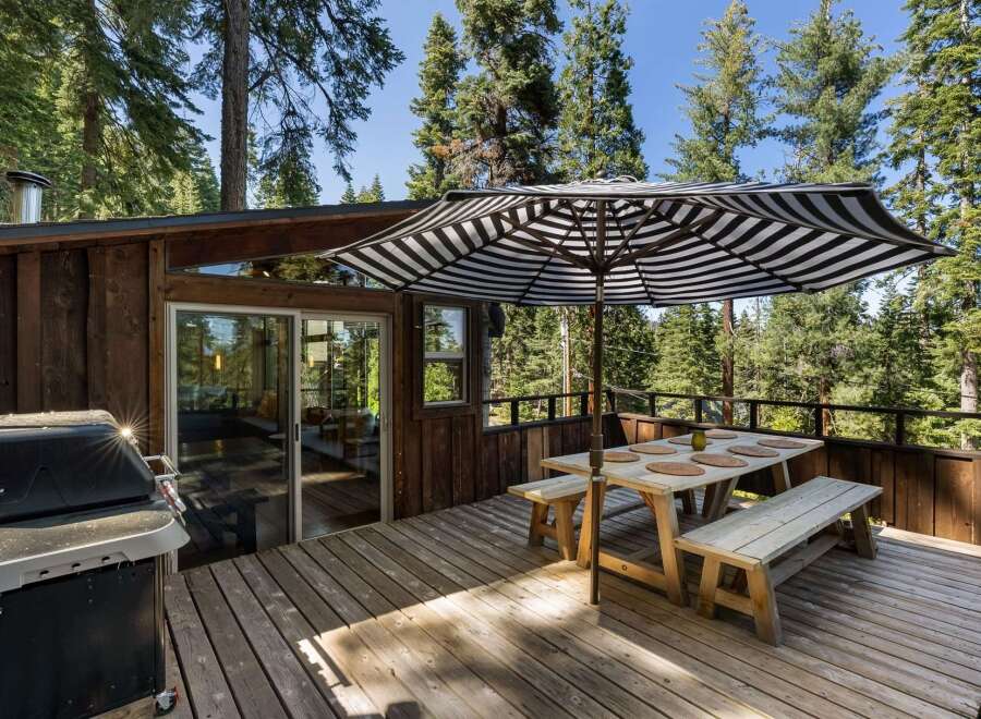 Enjoy outdoor dining and grilling on this spacious wooden deck, perfect for entertaining guests amidst a serene forest setting.