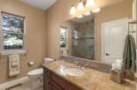 This beautifully appointed bathroom features a spacious vanity with a granite countertop and an undermount sink, complemented by a large mirror reflecting the elegant tiled shower.