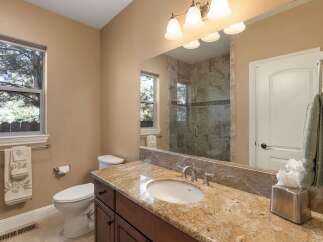 This beautifully appointed bathroom features a spacious vanity with a granite countertop and an undermount sink, complemented by a large mirror reflecting the elegant tiled shower.
