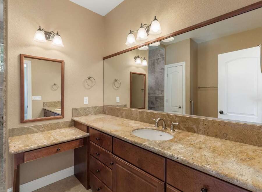 This spacious bathroom features a double vanity with granite countertops and rich wood cabinetry, offering ample storage.