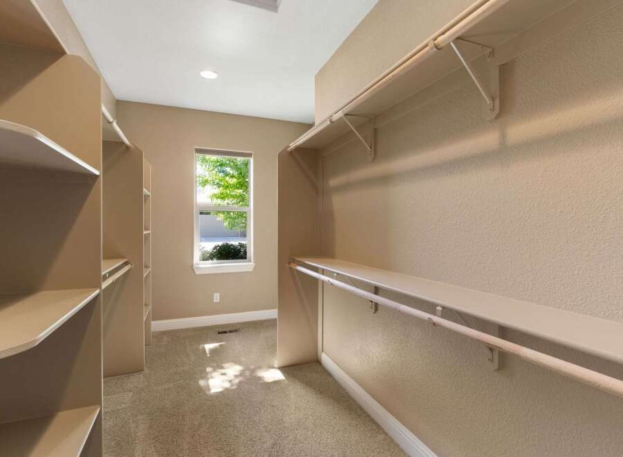 Discover ample storage in this spacious walk-in closet, featuring built-in shelving and multiple hanging rods.