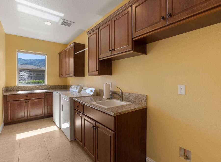 This spacious laundry room features ample storage with custom wood cabinetry and granite countertops.