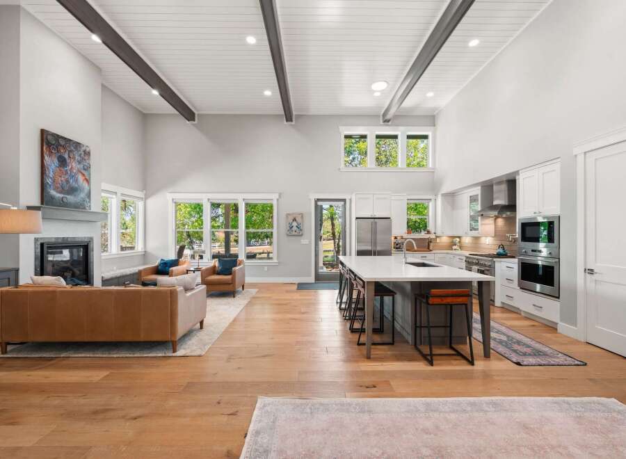 Experience modern luxury in this stunning open-concept living space, featuring a soaring vaulted ceiling with exposed beams and abundant natural light.
