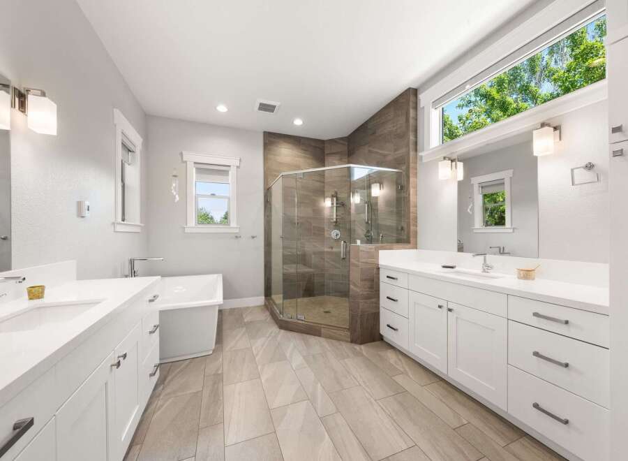 Experience luxury in this spacious master bathroom, featuring a freestanding soaking tub and a large, glass-enclosed walk-in shower with modern tilework.