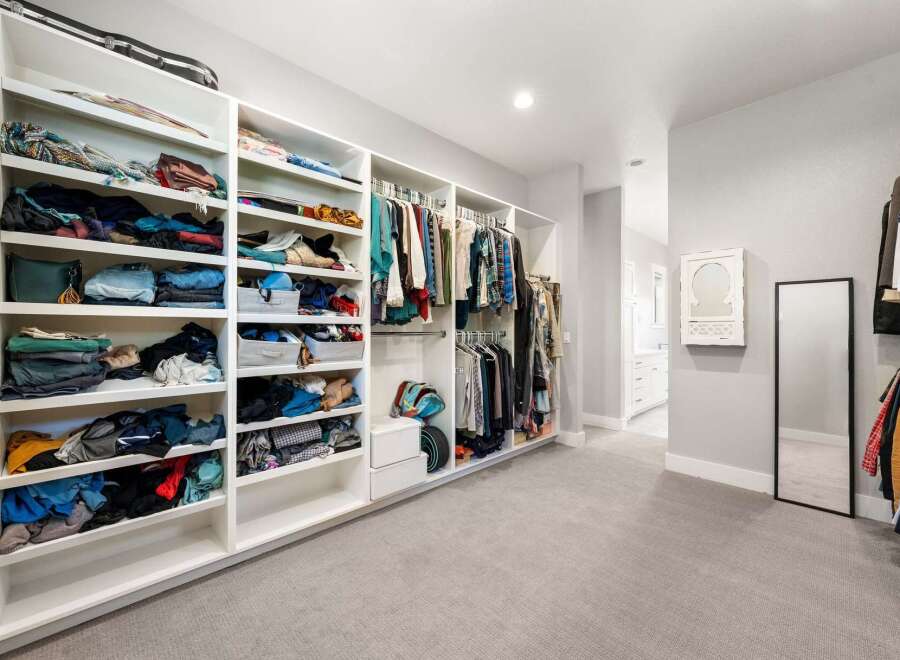 Discover ample storage in this spacious walk-in closet, featuring floor-to-ceiling shelving and multiple hanging racks to organize your wardrobe.