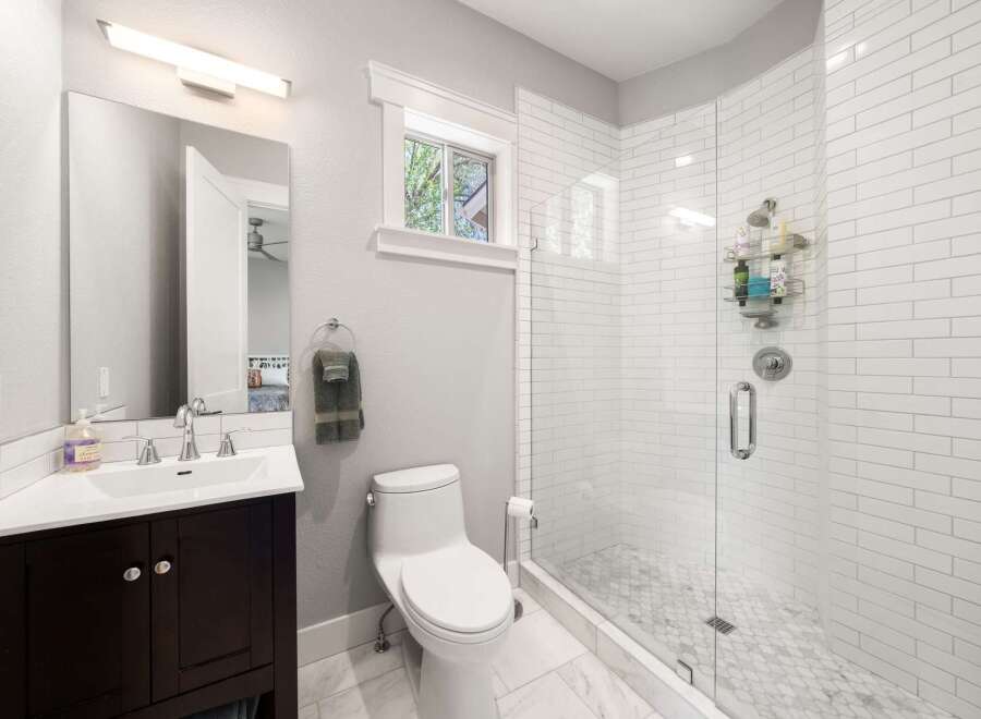 This modern bathroom features a sleek vanity with a white countertop and dark wood cabinets, complemented by a large mirror and a stylish vanity light.