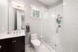 This modern bathroom features a sleek vanity with a white countertop and dark wood cabinets, complemented by a large mirror and a stylish vanity light.
