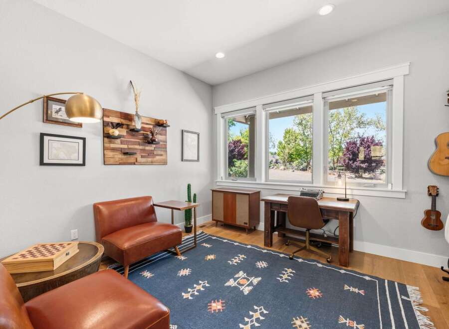 This home office features a cozy reading nook with a leather armchair and ottoman, complemented by a unique wooden wall art installation.