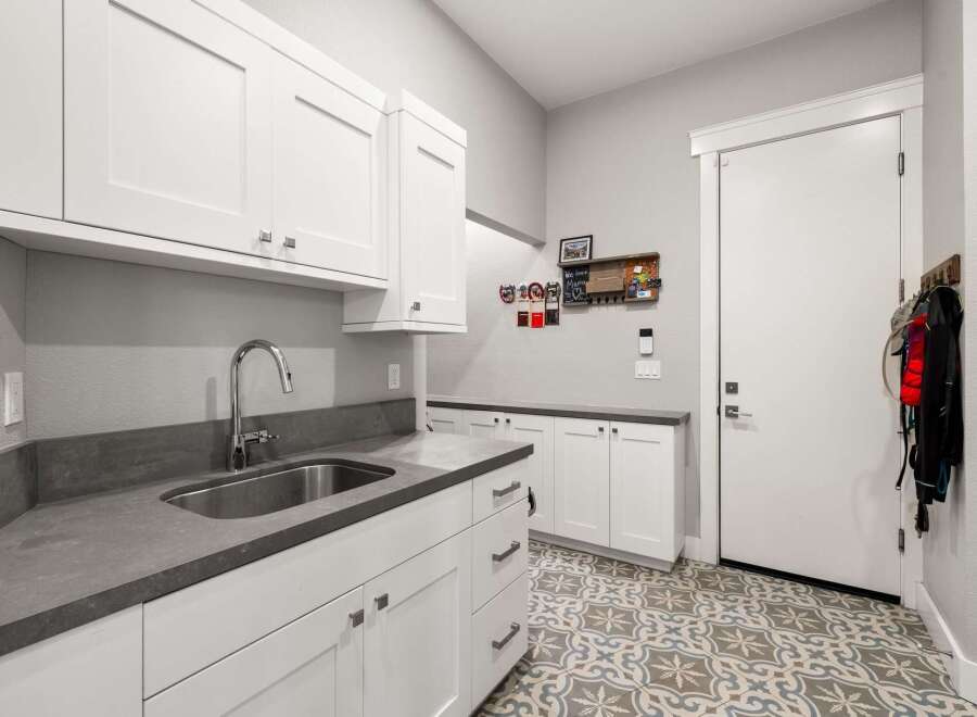 Discover this beautifully designed laundry room featuring crisp white cabinetry and sleek gray countertops.