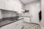 Discover this beautifully designed laundry room featuring crisp white cabinetry and sleek gray countertops.
