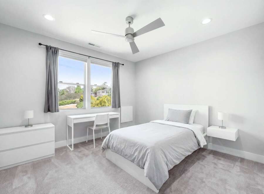 This modern bedroom features a comfortable bed with light gray bedding, a sleek white desk with a matching chair, and a minimalist dresser.