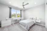 This modern bedroom features a comfortable bed with light gray bedding, a sleek white desk with a matching chair, and a minimalist dresser.
