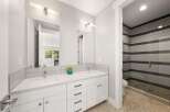 This modern bathroom features a spacious double vanity with white quartz countertops and sleek cabinetry, complemented by a stylish tiled shower enclosure with horizontal gray and white accents.