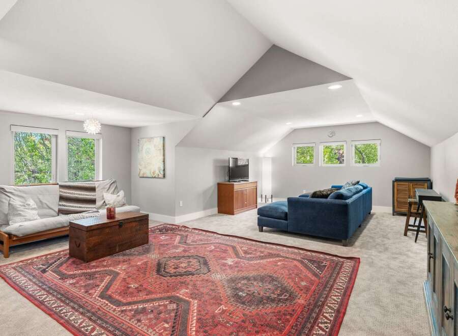 This spacious living area features a large, ornate Persian rug that anchors the room, complemented by a comfortable blue sectional sofa and a wooden futon.