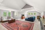 This spacious living area features a large, ornate Persian rug that anchors the room, complemented by a comfortable blue sectional sofa and a wooden futon.