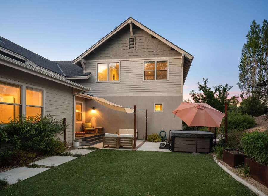 Enjoy outdoor living with this charming backyard featuring a relaxing hot tub and a cozy seating area under a shade sail.