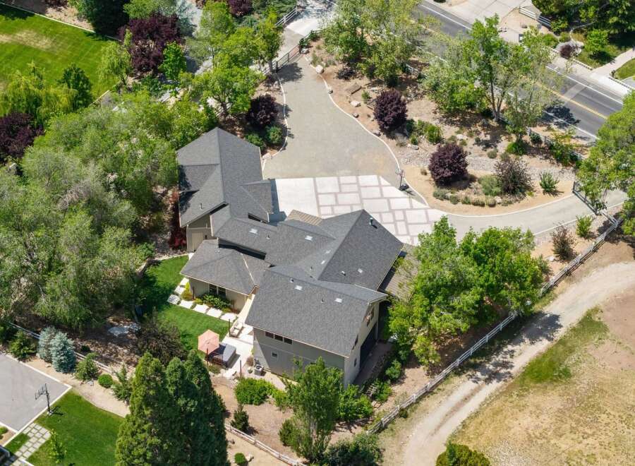 Discover this stunning property featuring a spacious, multi-level home with a dark shingle roof, nestled amidst lush greenery and mature trees.