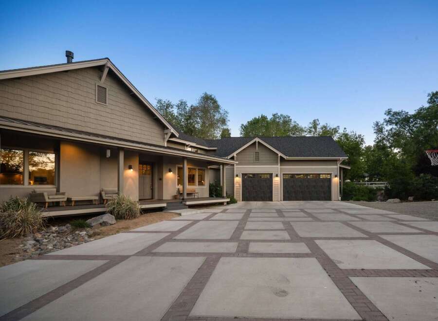 This stunning property features a spacious driveway with a unique concrete and brick paver design, leading to a large attached garage.