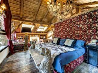 Experience rustic luxury in this charming bedroom featuring a grand wooden-beamed ceiling and a stunning crystal chandelier.