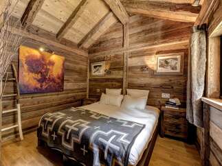 Experience rustic charm in this cozy wooden bedroom, featuring a comfortable bed adorned with a stylish geometric blanket.