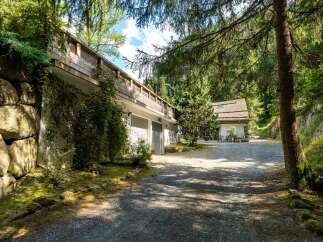 Nestled in a serene forest setting, this property features a unique multi-level design with a striking stone wall and a wooden balcony.