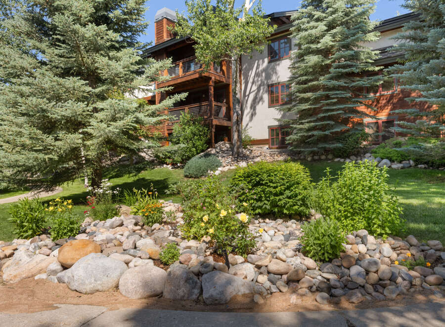 Experience mountain living in this stunning property, featuring a beautiful natural stone landscaping with vibrant yellow roses and lush greenery.
