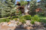 Experience mountain living in this stunning property, featuring a beautiful natural stone landscaping with vibrant yellow roses and lush greenery.
