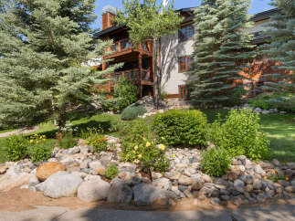 Experience mountain living in this stunning property, featuring a beautiful natural stone landscaping with vibrant yellow roses and lush greenery.