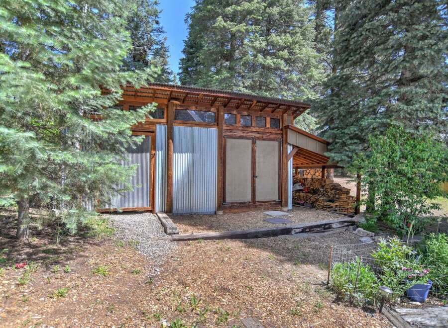 Discover this unique property featuring a rustic-modern shed with corrugated metal siding and a sloped wooden roof, nestled amongst mature pine trees.