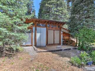 Discover this unique property featuring a rustic-modern shed with corrugated metal siding and a sloped wooden roof, nestled amongst mature pine trees.