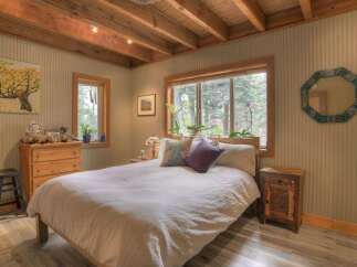Experience cozy cabin living in this charming bedroom, featuring a comfortable bed adorned with plush pillows and a white duvet.